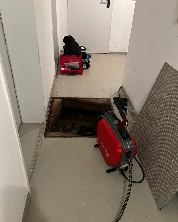 Rohrreinigungsmaschine vor einer geöffneten Revisionsöffnung in einem Hausflur